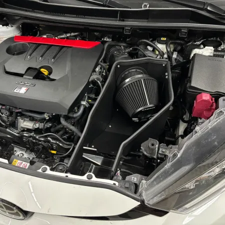 Gros plan sur le compartiment moteur d'une Toyota GR Yaris, mettant en avant le kit d'admission RamAir Proram. On voit le filtre à air, le bouclier thermique et le tuyau d'admission. Intégration parfaite.