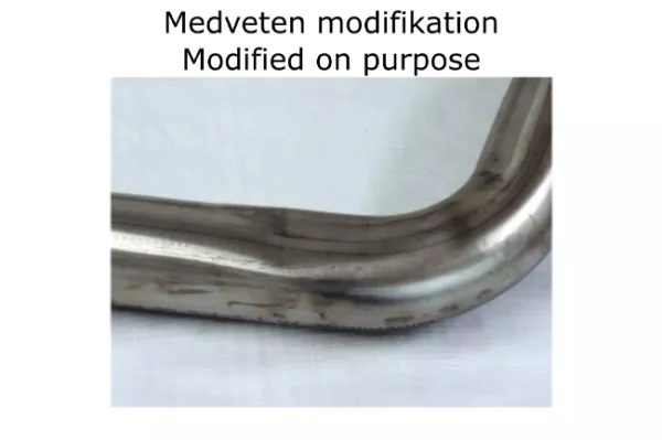 Gros plan sur un tube coudé en acier inoxydable pour échappement sport Simons. Tube argenté brillant avec légères traces d'usage. «Medveten modifikation Modified on purpose» au-dessus. Pièce pour BMW F30 320i/328i.